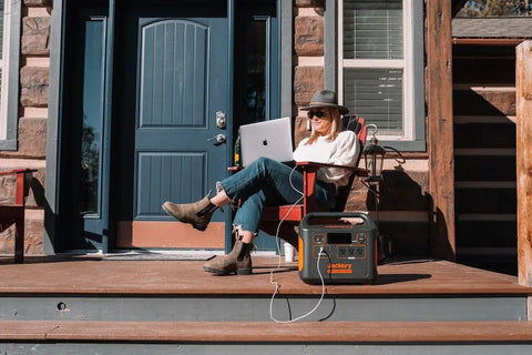 Woman on her front porch working on a laptop while charging it using a Jackery solar generator